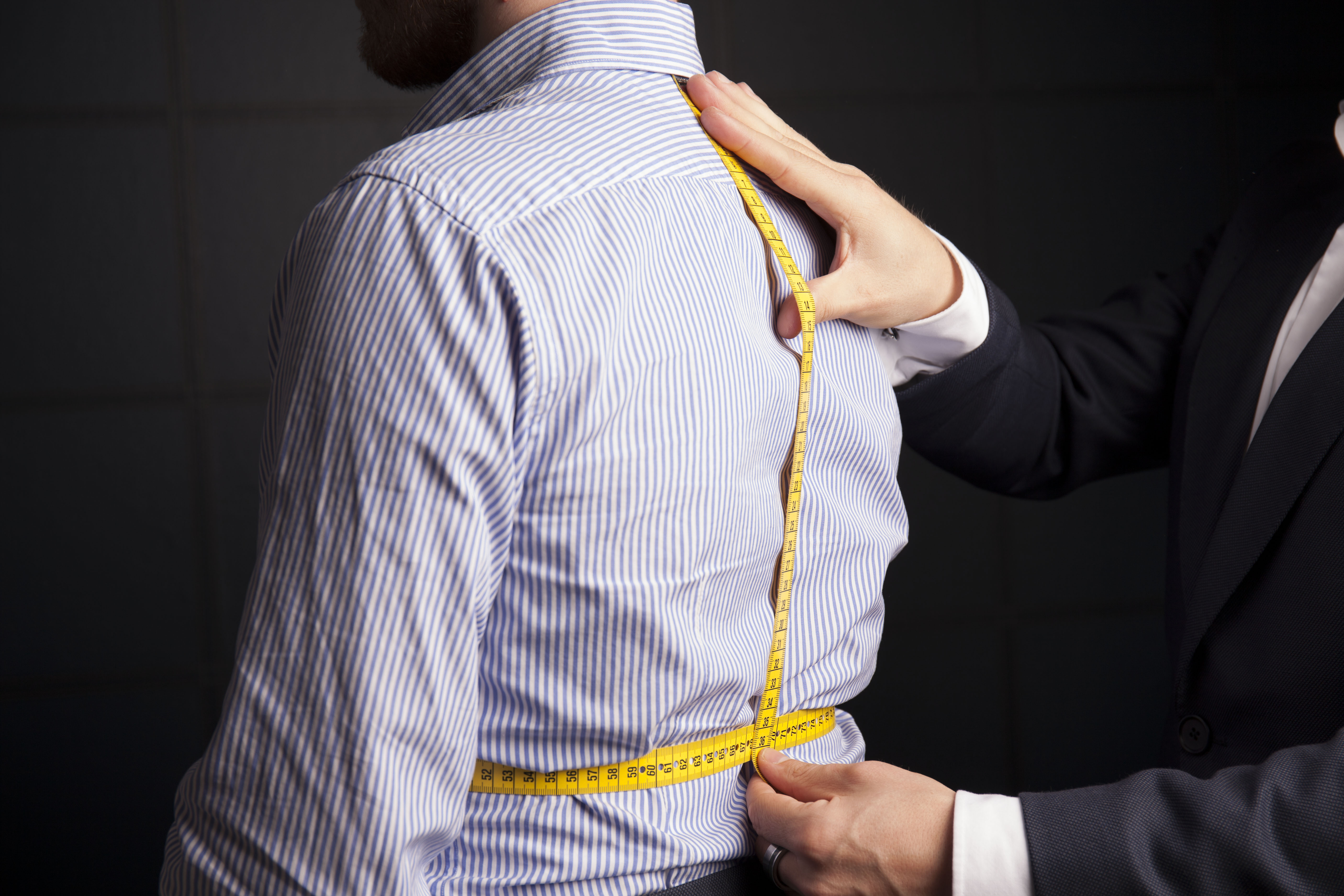 A tailor running a measuring tape down the back of a striped dress shirt