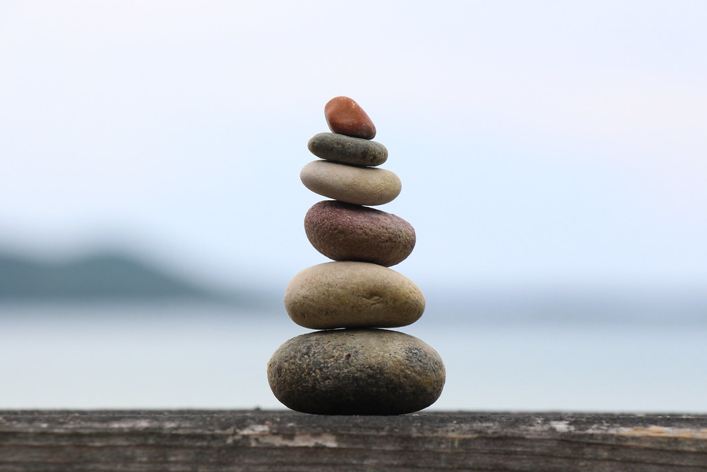 Stones stacked in balance on a wooden rail, largest at the bottom