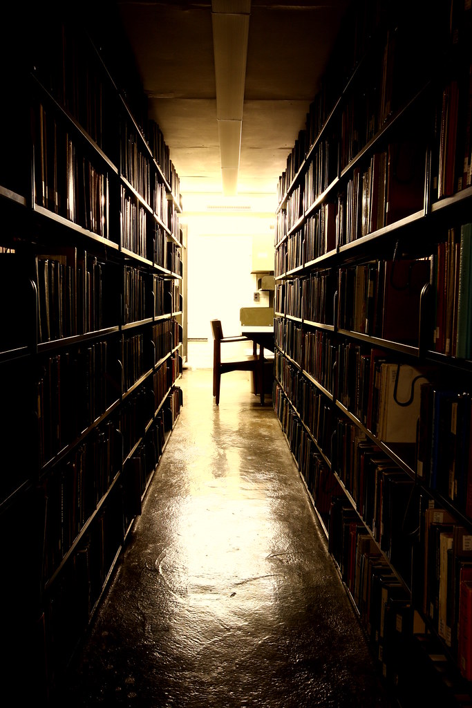 A dark library aisle with light at the far end