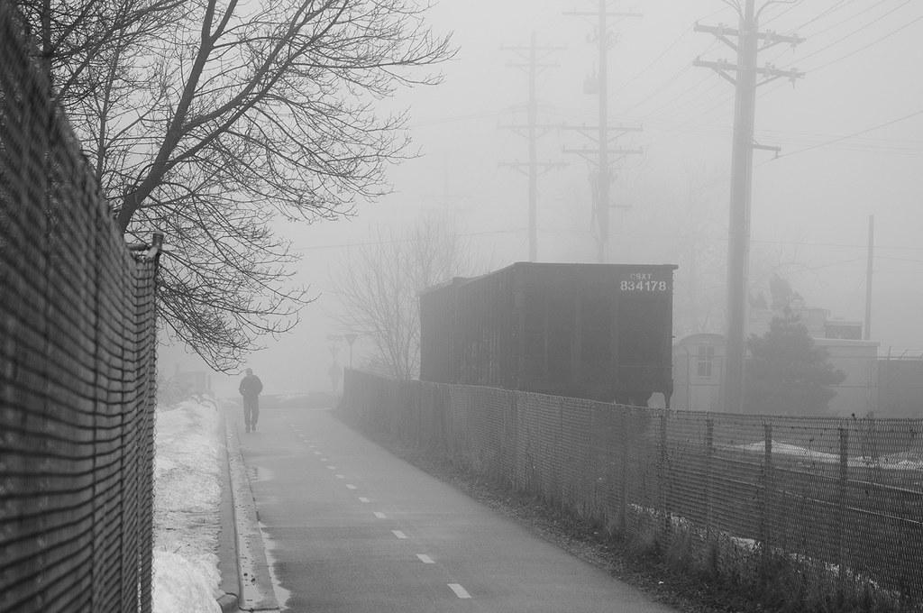 A lone figure walking a foggy path beside a freight car