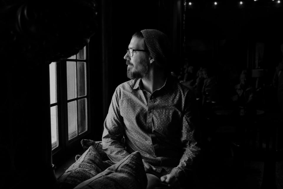 A man sitting by a window in a dark room, black and white