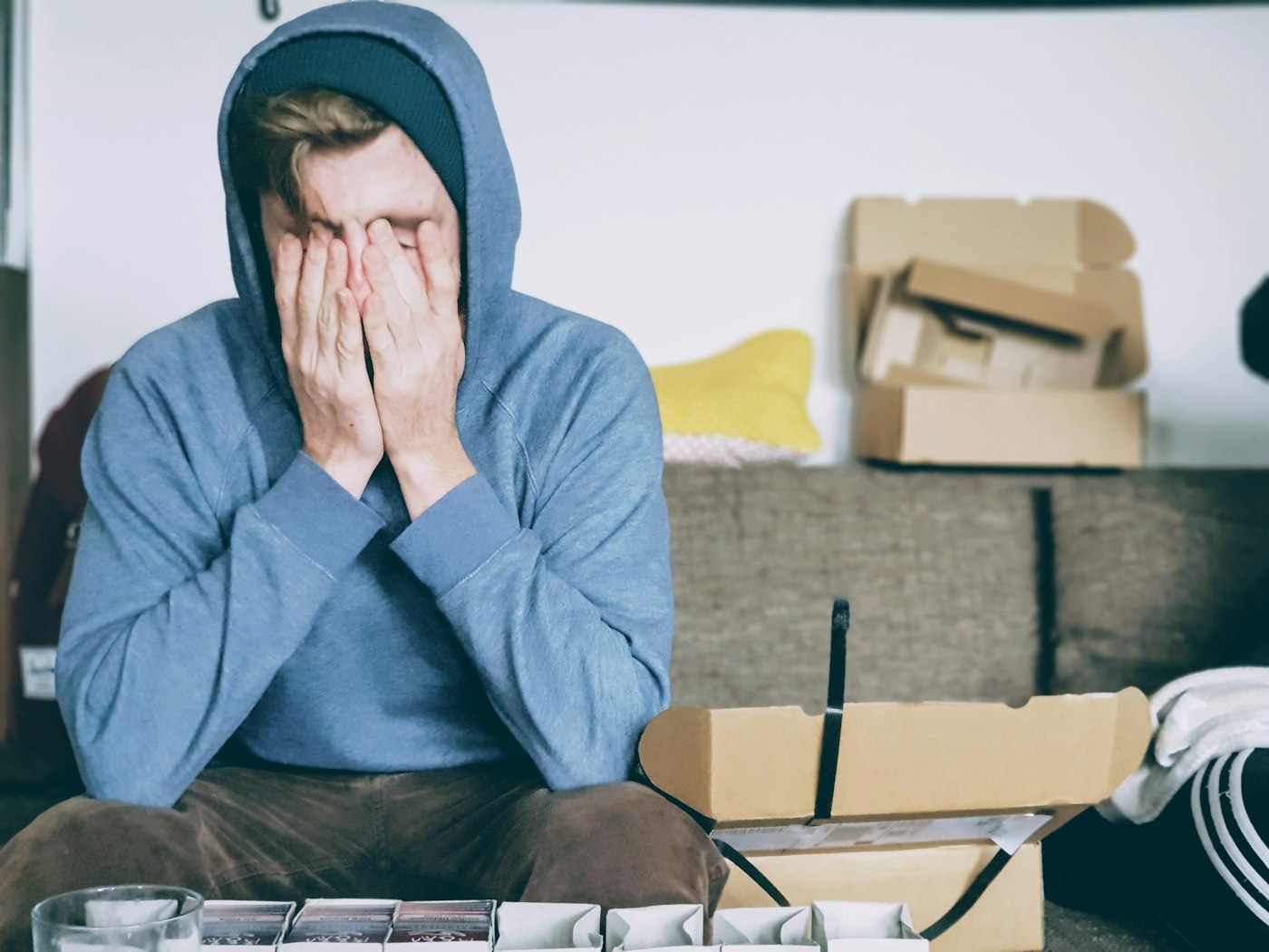 A young man in a hoodie covering his face with both hands